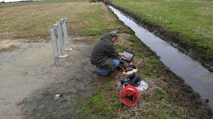 Researcher using instruments in the field beside a drainage ditch. 