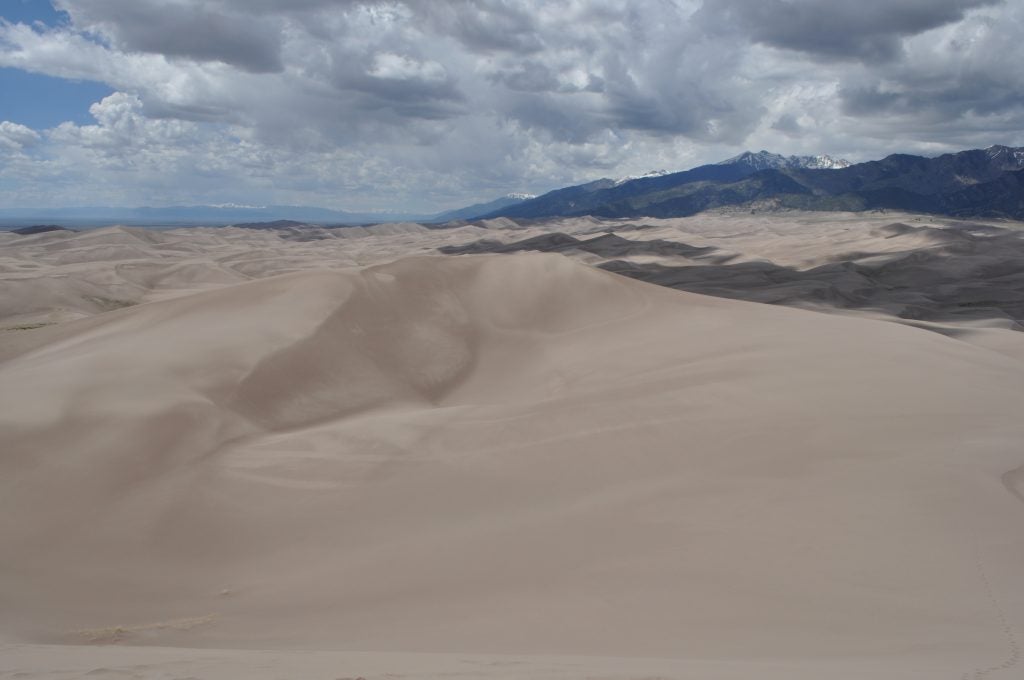 Expansive sand dunes leading up to snow-capped mountain peaks.